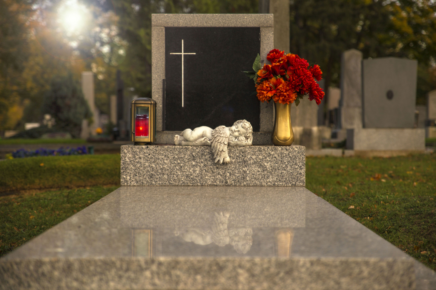 Grab mit Grabplatte, Blumenvase und Kerze. Ein Engel aus Stein liegt auf der Platte.