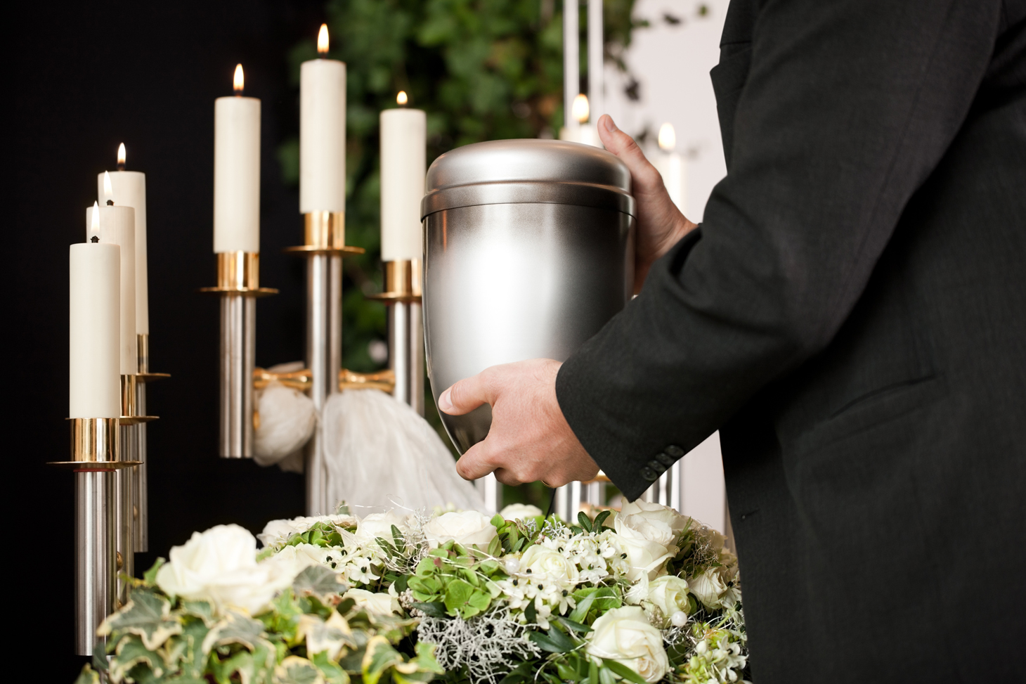 Eine Urne wird vor Kerzen und Blumenschmuck in der Hand gehalten.